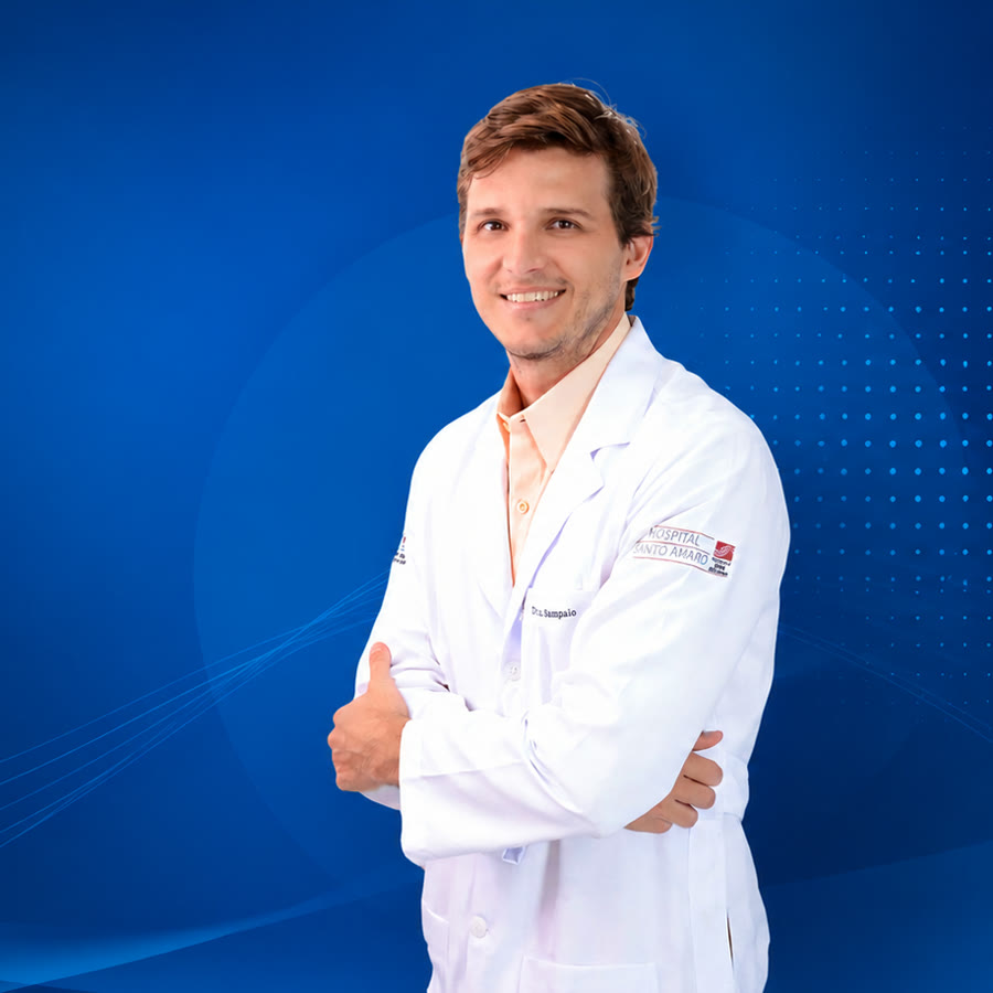 Dr. Luiz Sampaio de jaleco branco e camisa salmão, sorrindo, de braços cruzados